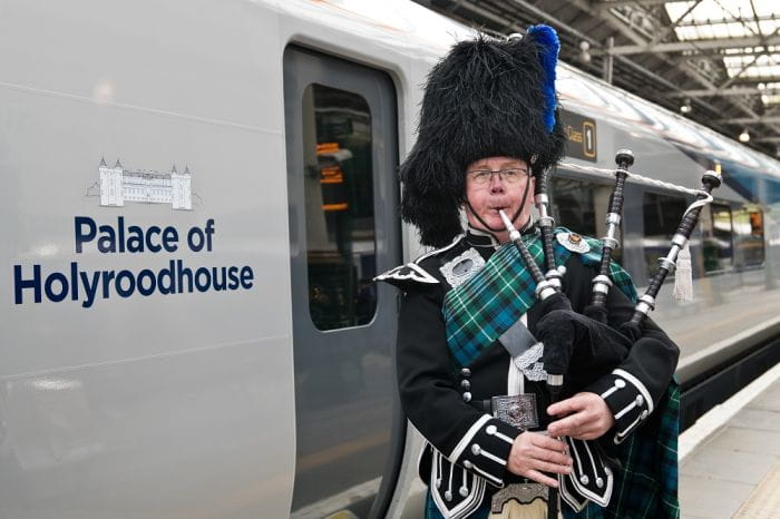 A man playing the bagpipes stood next to a train on the platform