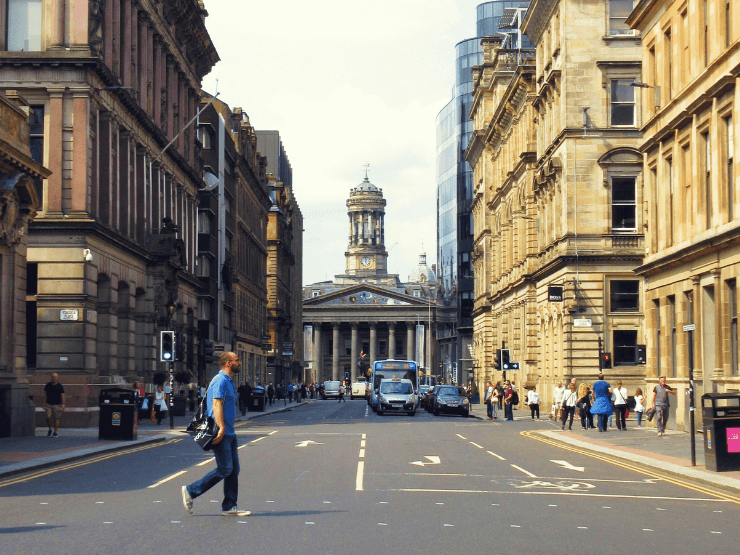 The city of Glasgow with a man walking over a zebra crossing and architectural landmarks visible in the background