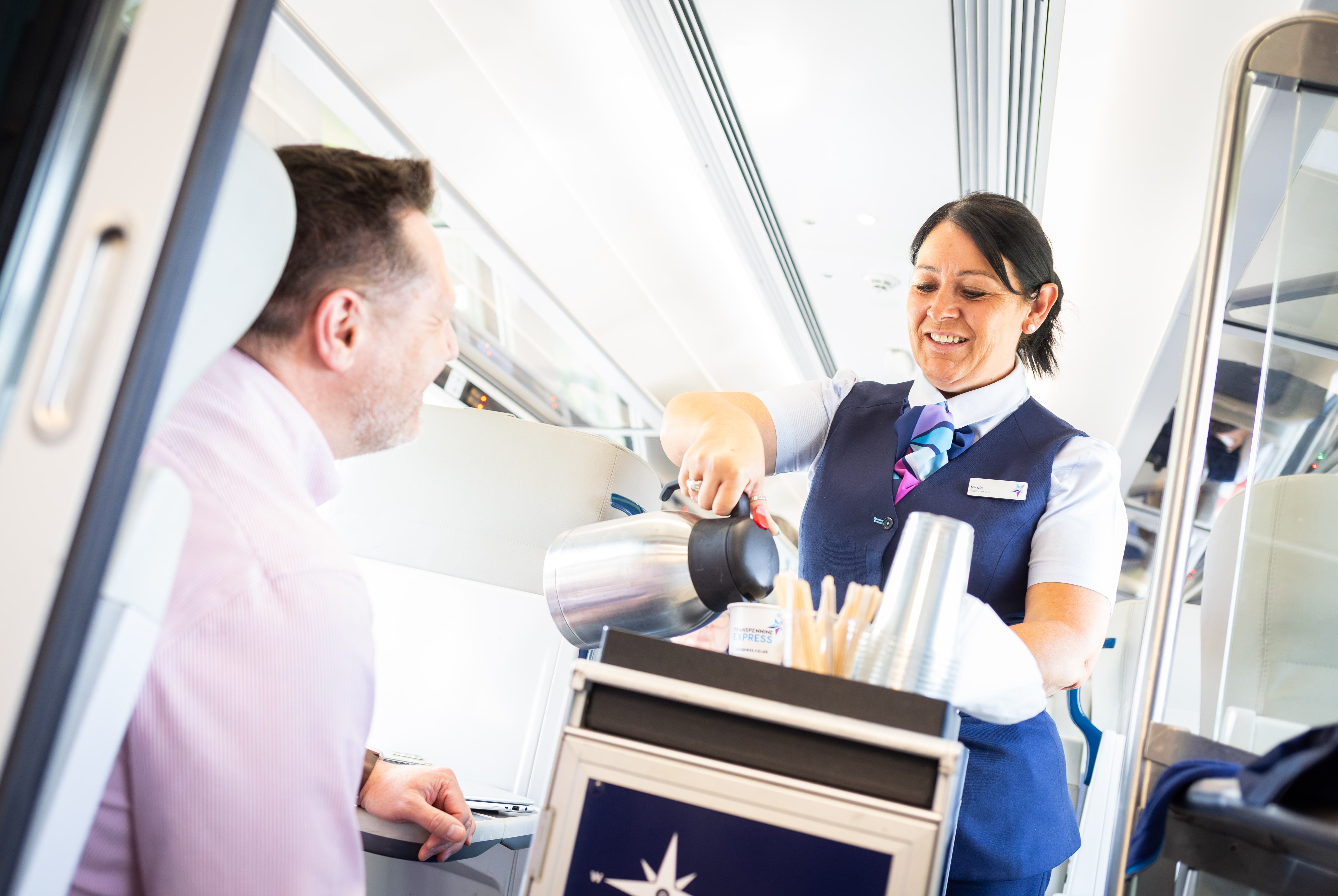 A TransPennine Express customer host pouring a gentleman a hot drink from the catering trolly on the train