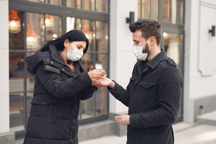 Man and woman in masks using hand sanitizer 
