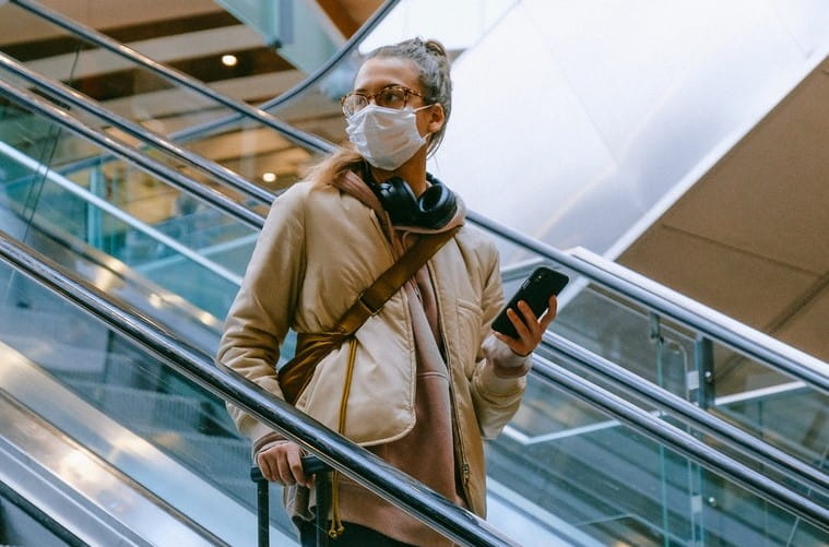 Woman in mask on escalator with mobile phone