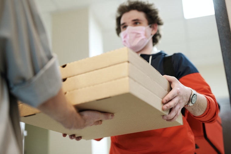 Delivery man wearing mask handing over pizza boxes