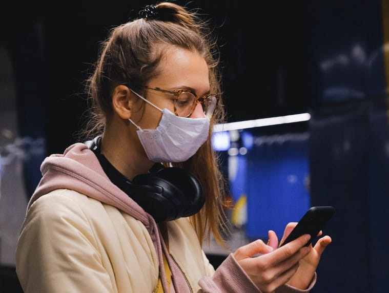 Woman wearing facemask using mobile phone on a train platform