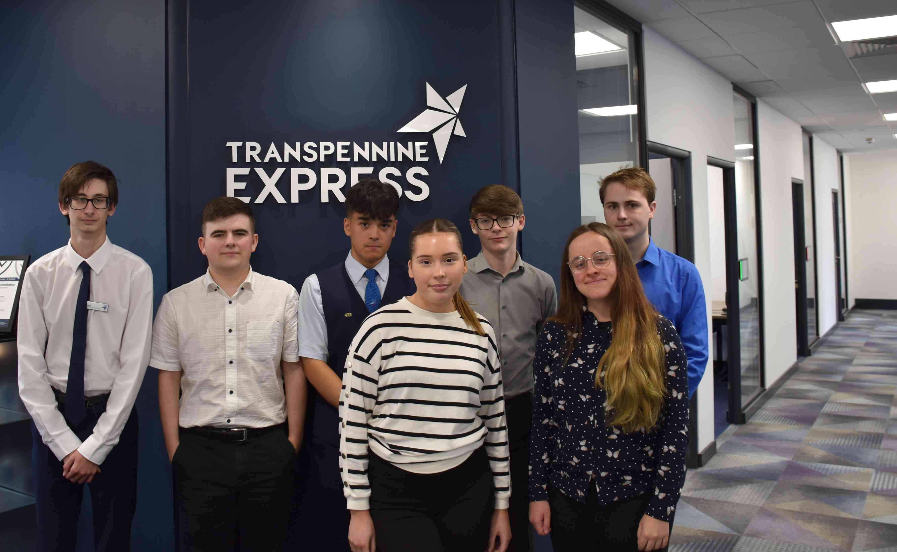 7 TransPennine Express apprentices stood in a line in front of a TransPennine Express sign